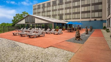 Une cour d’hôtel avec des chaises longues, un espace salon abrité et un bâtiment doté de grandes fenêtres.