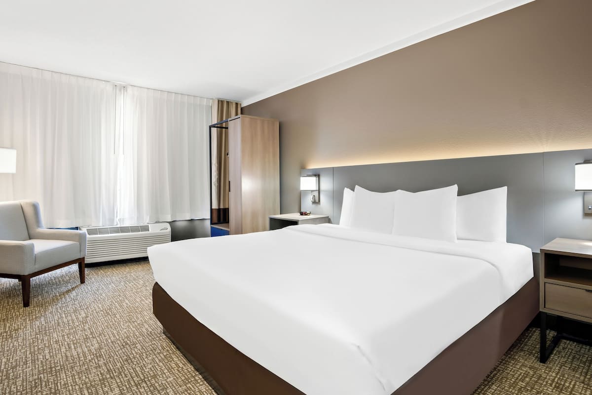 A hotel room with a large bed, a chair, a bedside table, and a wall-mounted lamp.