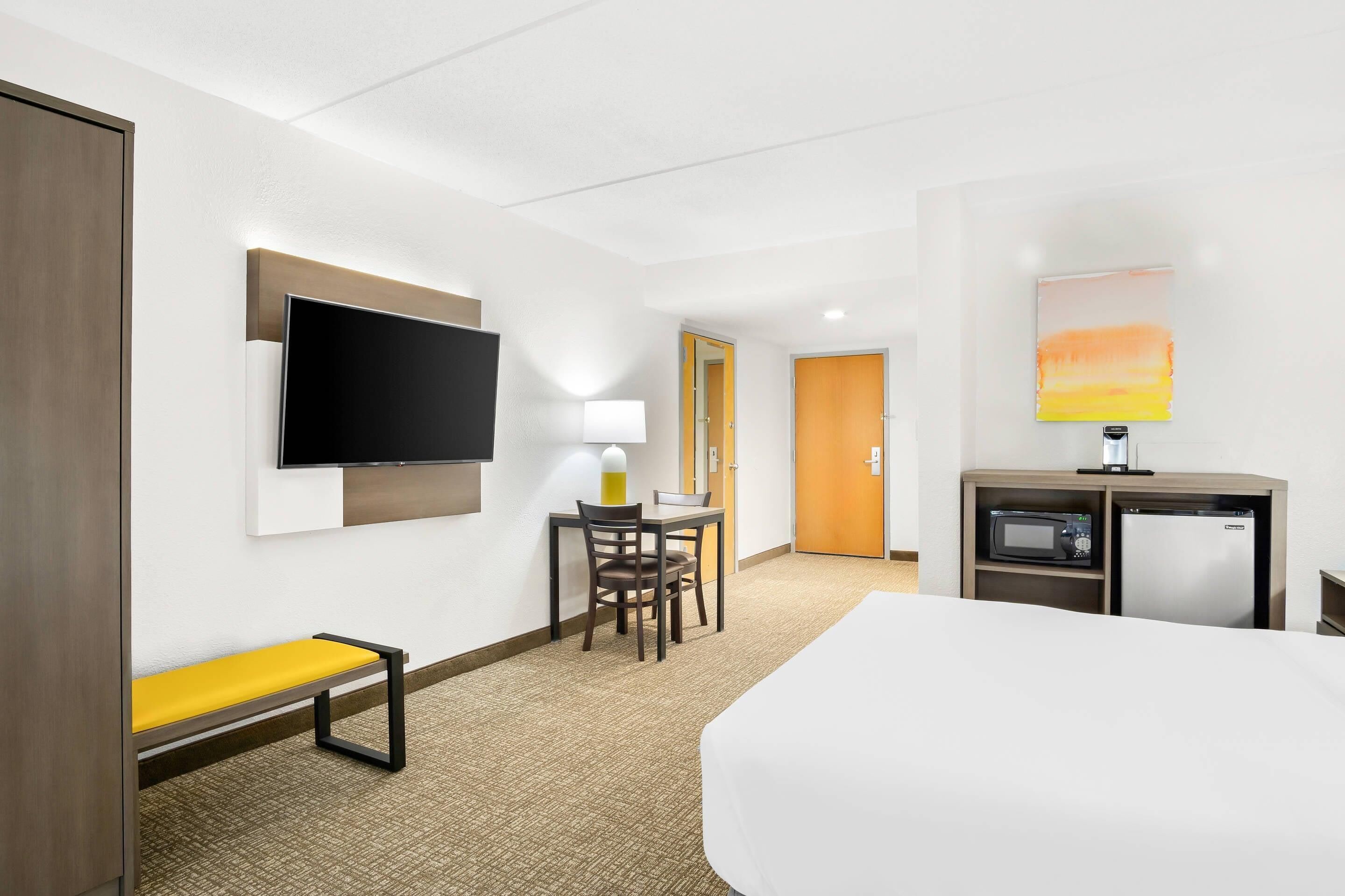 Una habitación de hotel con una cama, un escritorio con una silla, un televisor, un microondas y un mueble pequeño.