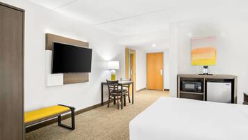 Una habitación de hotel con una cama, un escritorio con una silla, un televisor, un microondas y un mueble pequeño.