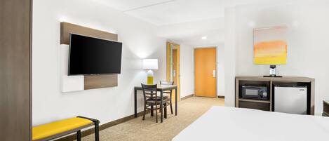 Una habitación de hotel con una cama, un escritorio con una silla, un televisor, un microondas y un mueble pequeño.