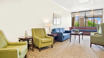 A hotel lobby with a patterned carpet, green and blue sofas, and a large window with a city view.