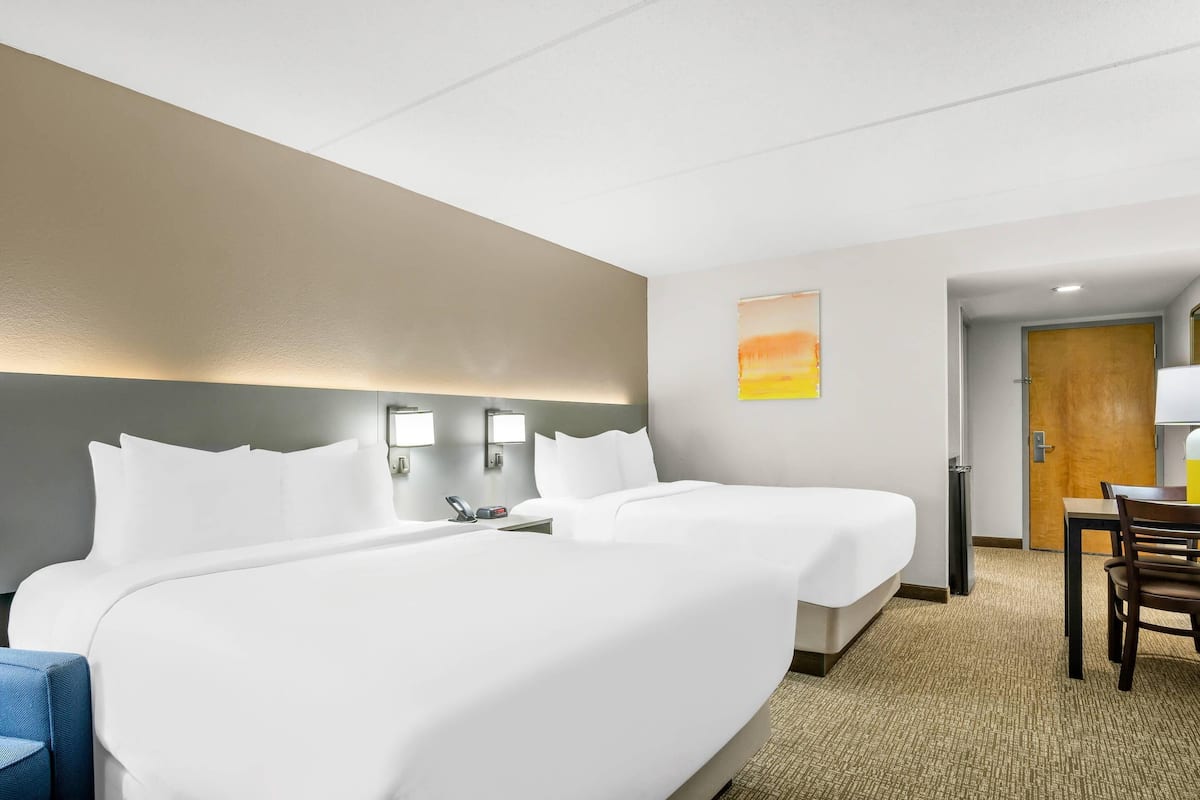A hotel room with two beds, a desk, a chair, and a painting on the wall.