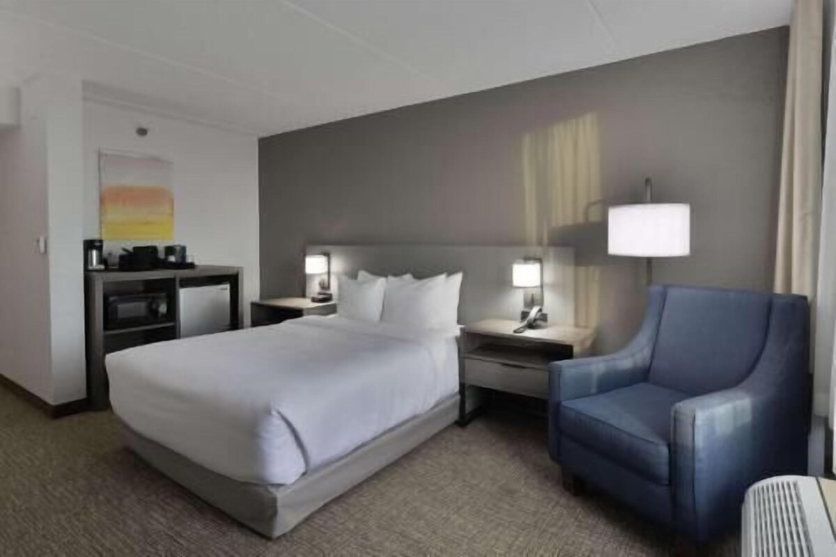 A hotel room with a bed, a desk with a computer, a chair, and a lamp.