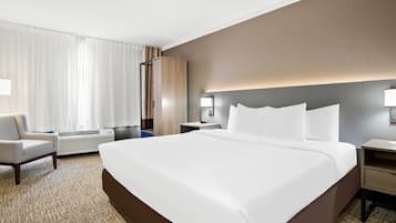 Una habitación de hotel con una cama grande, una silla, una mesita de noche y una lámpara de pared.