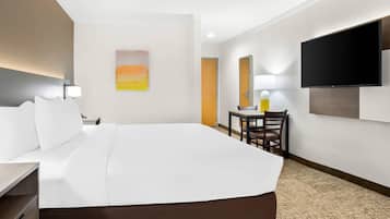 A hotel room with a large bed, a desk, a chair, a flat-screen TV mounted on the wall, and a painting on the wall.