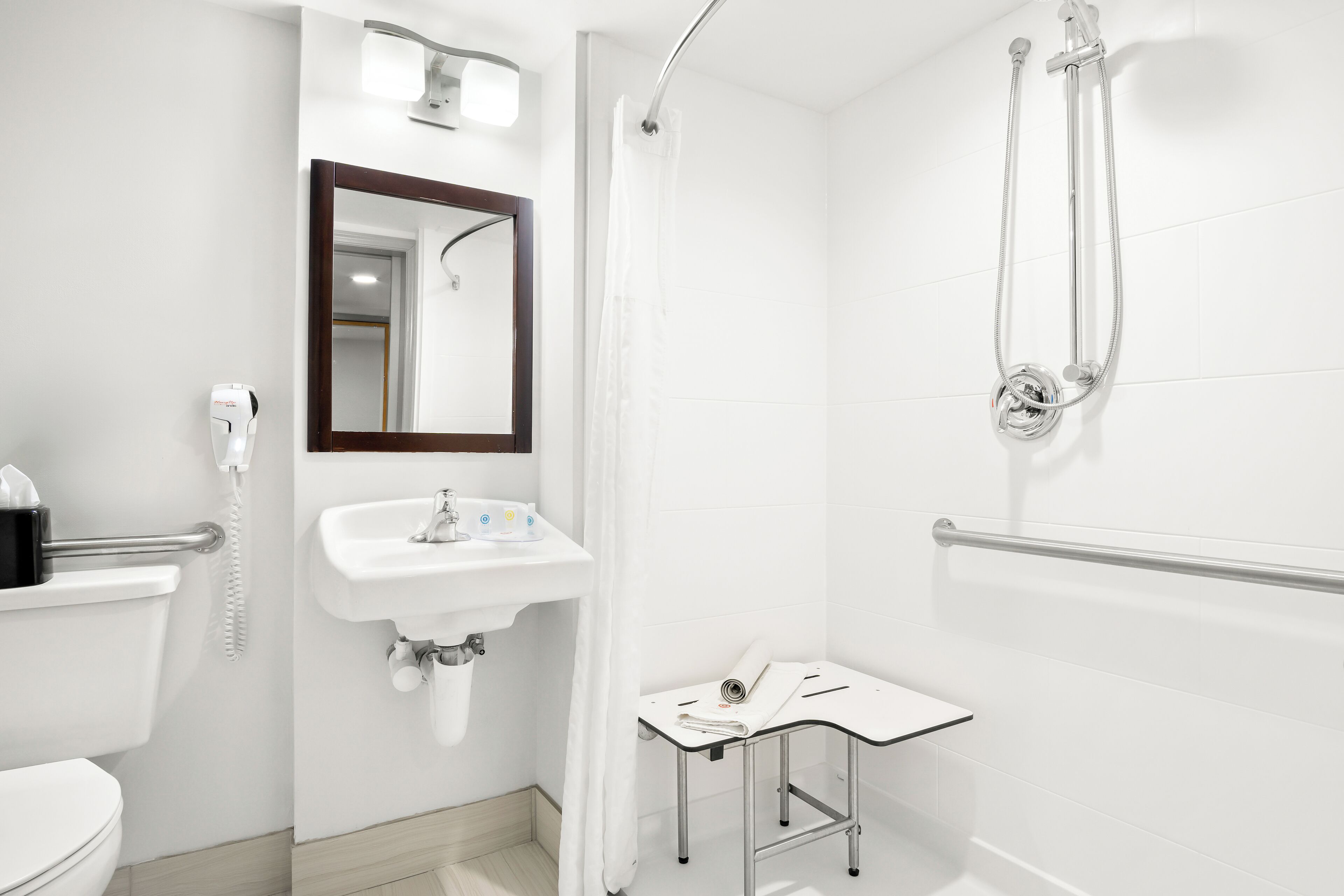 Un baño moderno con inodoro, lavamanos, espejo, ducha y una mesita con una toalla.