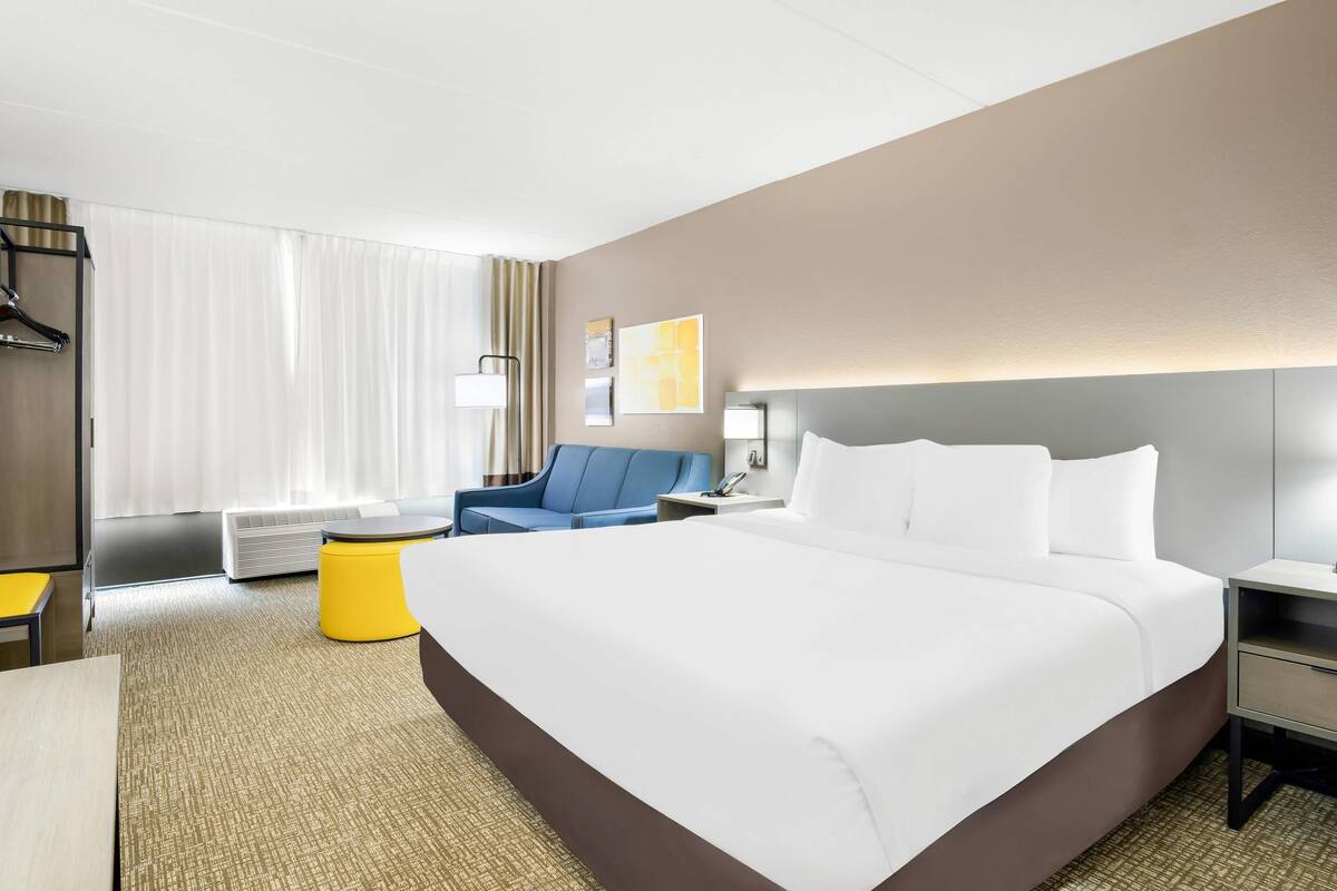 A hotel room with a large bed, a desk, a chair, a small table, and a window with curtains.