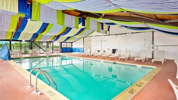 Una piscina interior con superficie de agua cristalina, rodeada de sillas de descanso y un techo con cortinas de colores.