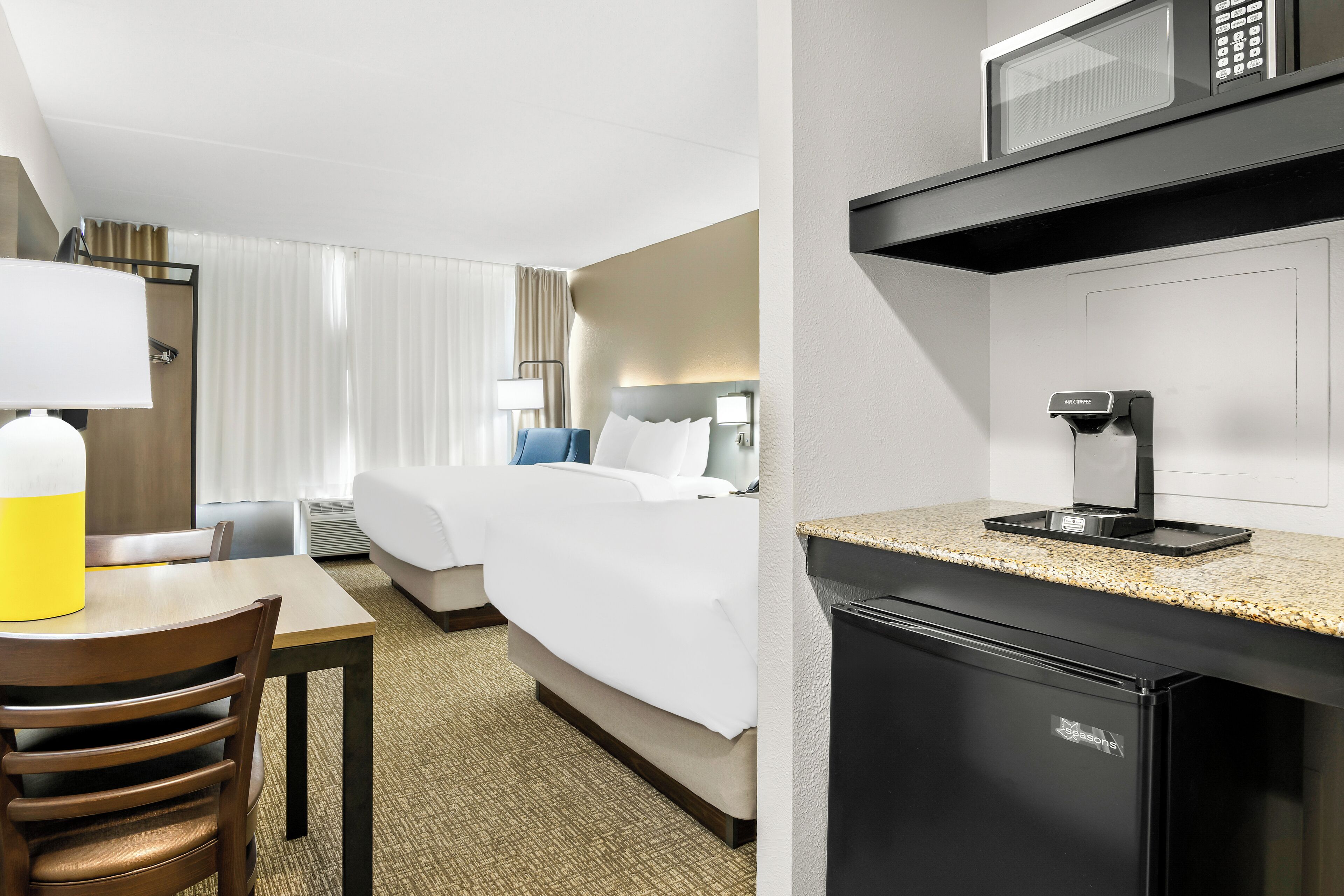 A hotel room with a bed, a desk with a lamp, a microwave, and a coffee maker.