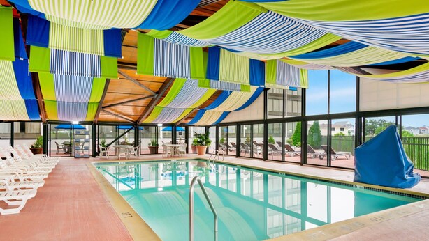 An indoor swimming pool with clear glass walls, lounge chairs, and a view of the outside. - Comfort Inn Gold Coast (Ocean City)