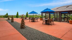 An outdoor patio with tables and chairs, blue umbrellas, and potted plants. - Comfort Inn Gold Coast (Ocean City)