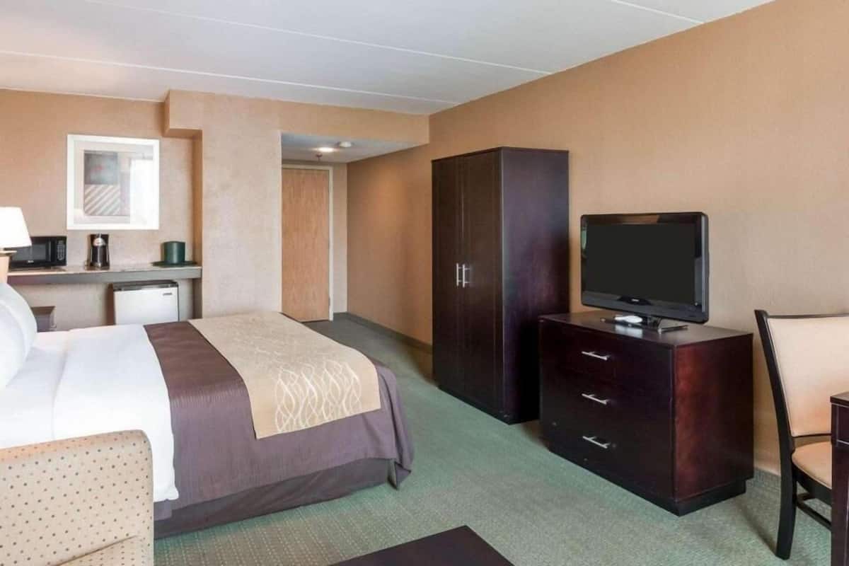 A hotel room with a bed, a television on a dresser, a desk with a lamp, and a microwave.