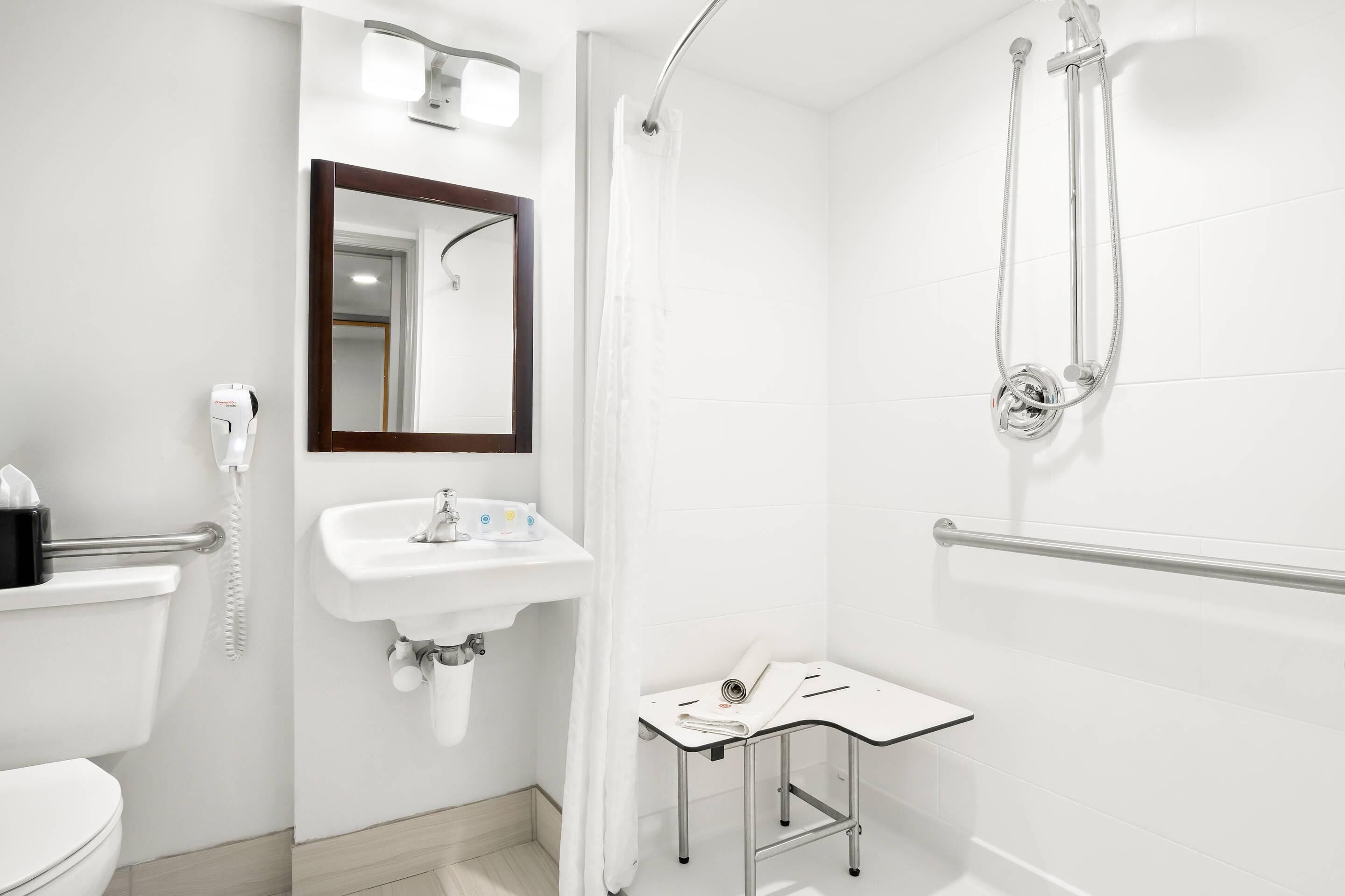 A modern bathroom with a toilet, sink, mirror, shower, and a small table with a towel.