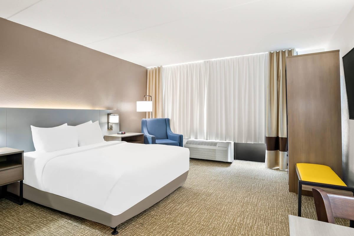 A hotel room with a large bed, a desk, a chair, a lamp, and a window with curtains.
