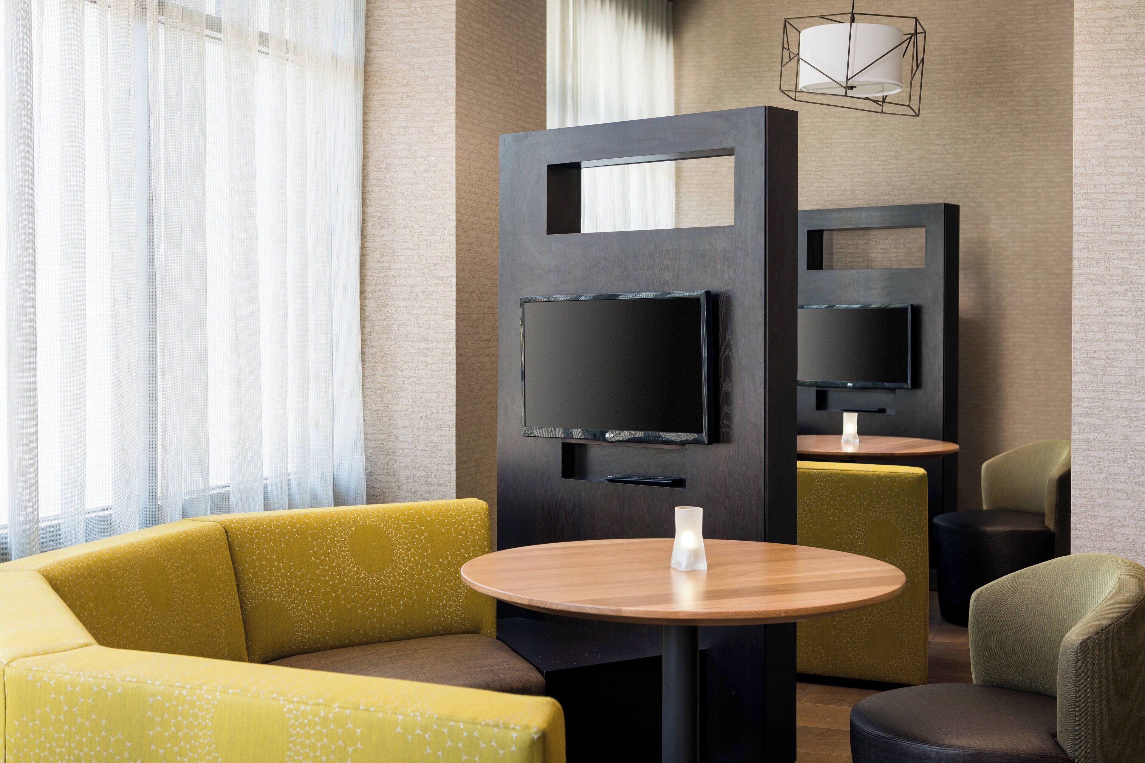 A modern hotel room with a sofa, a round table, and a TV mounted on a wall.