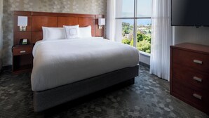A hotel room with a large bed, a TV, a nightstand, and a view of the outdoors. - Courtyard by Marriott Richmond/Berkeley (San Pablo)