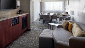 A hotel room with a kitchenette, a dining area, and a living area with a sofa and ottoman. - Courtyard by Marriott Richmond/Berkeley (San Pablo)