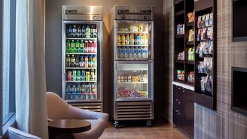 A hotel lobby with two beverage vending machines, a seating area, and a magazine rack.