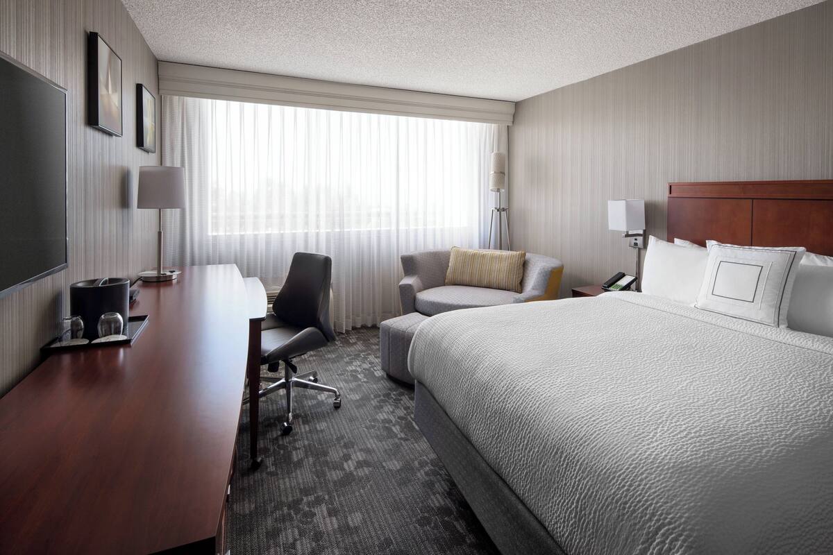 A hotel room with a large bed, a desk with a chair, a small sofa, and a TV.