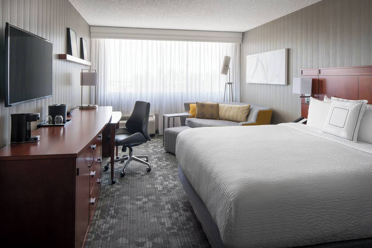 A hotel room with a large bed, a desk with a chair, a television, and a window with curtains.