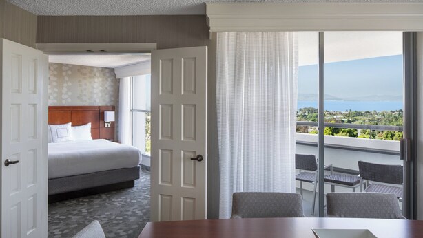 A hotel room with a bed, a dining table, and a balcony with a view. - Courtyard by Marriott Richmond/Berkeley (San Pablo)