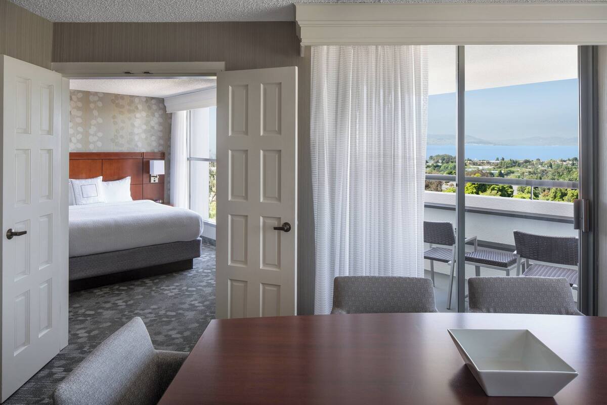 A hotel room with a bed, a dining table, and a balcony with a view.