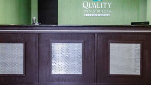 A reception area with a green wall, a logo for 'Quality Inn & Suites by Choice Hotels', and a dark wooden counter with a metal grate. - Quality Inn & Suites Medina - Akron West (Medina)