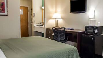A hotel room with a bed, desk, chair, microwave, and a TV on the wall.