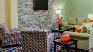 A living room with a stone wall, a flat-screen TV, patterned sofas, and a coffee table. - Quality Inn & Suites Medina - Akron West (Medina)