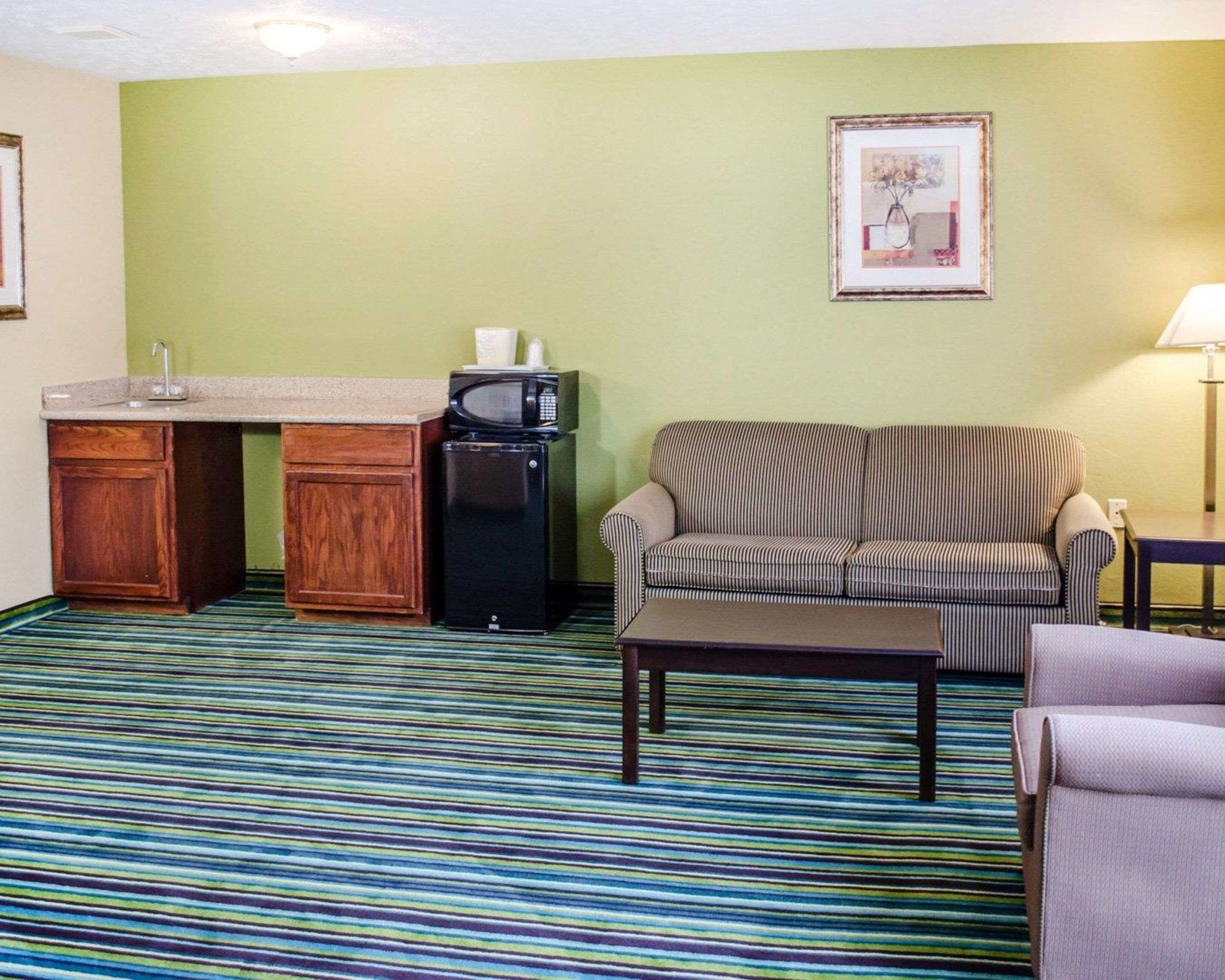 Quarto de hotel compacto com cozinha americana, sofá listrado, uma pequena mesa e um quadro na parede.