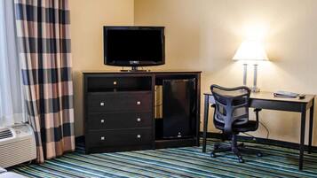 Habitación de hotel con televisión, escritorio con lámpara, una silla, cómoda y alfombra a rayas.