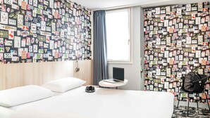Una habitación de hotel con una cama, una mesita redonda con un ordenador portátil, una silla y una pared decorada con tarjetas.