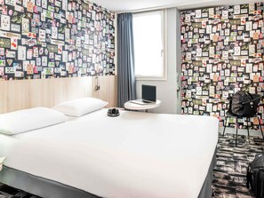 A hotel room with a bed, a small round table with a laptop, a chair, and a wall covered with cards. - ibis Styles Reims Centre Cathédrale (Reims)