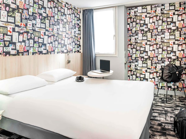 A hotel room with a bed, a small round table with a laptop, a chair, and a wall covered with cards. - ibis Styles Reims Centre Cathédrale (Reims)