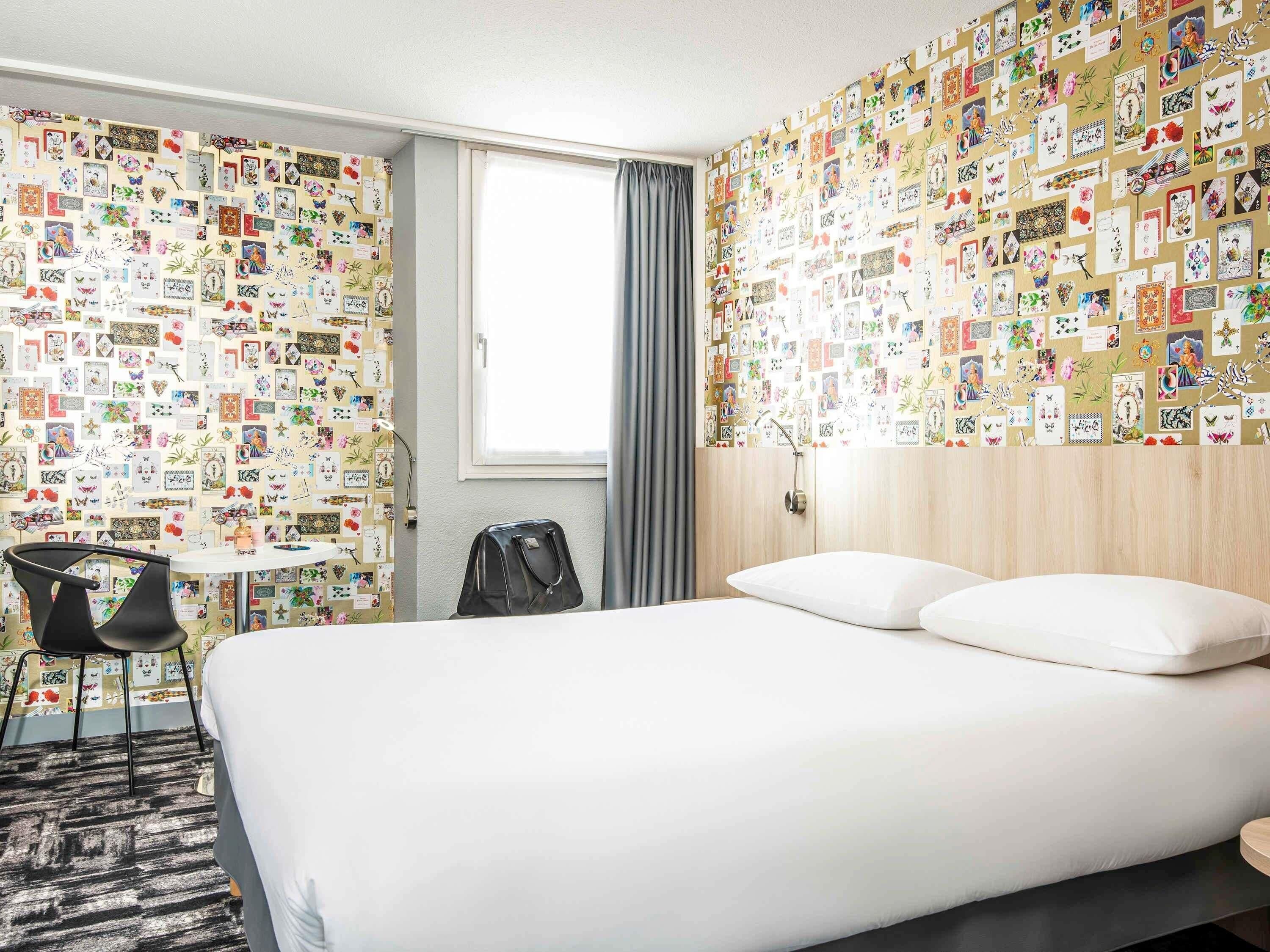 A hotel room with a bed, a desk, a chair, and a wall covered with various pictures.