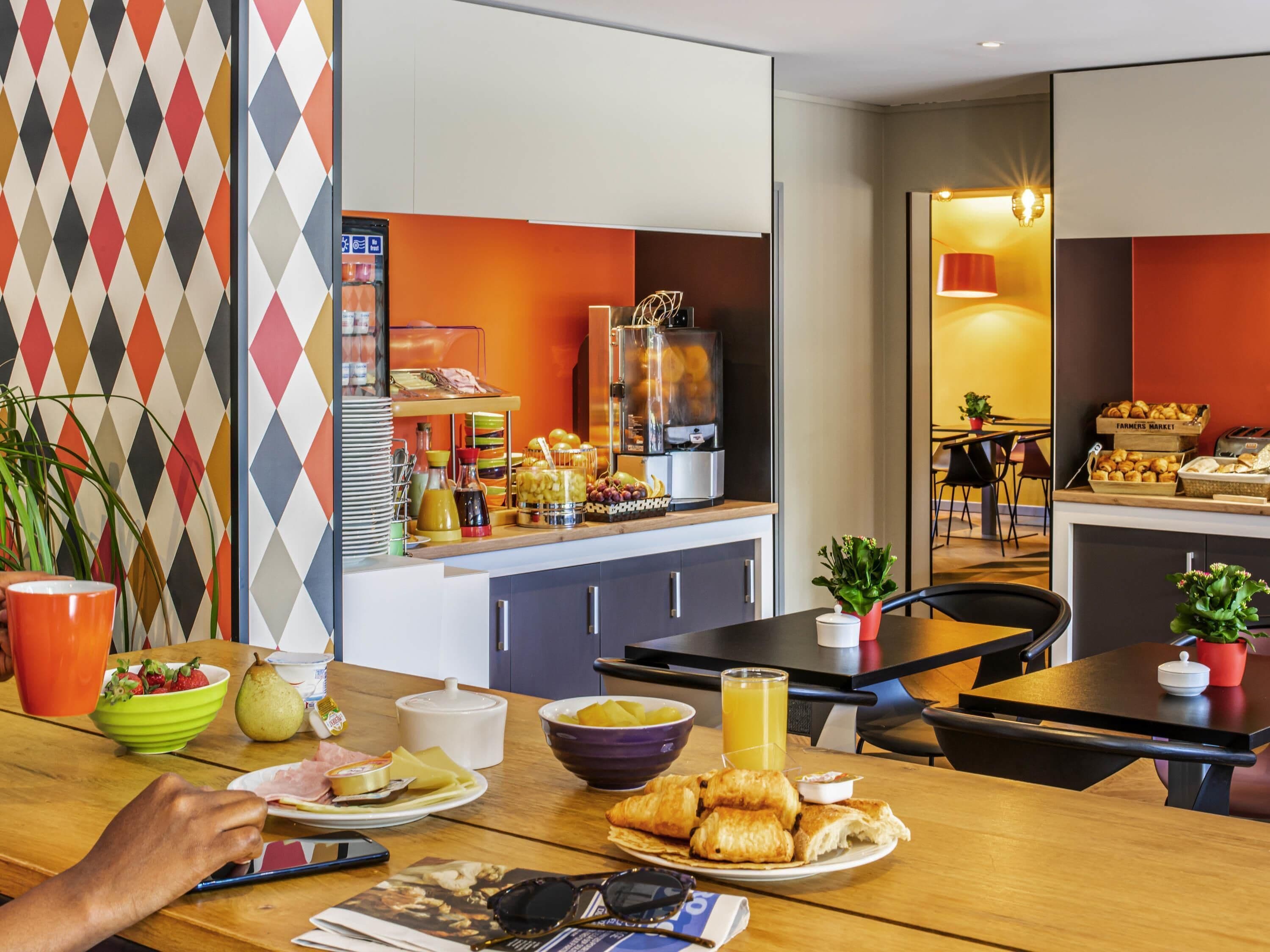 A breakfast setup with a variety of food items, a coffee machine, and a dining area with chairs and a table.