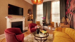 A living room with a fireplace, red and yellow armchairs, a sofa, a flat-screen TV, and a large window with curtains.