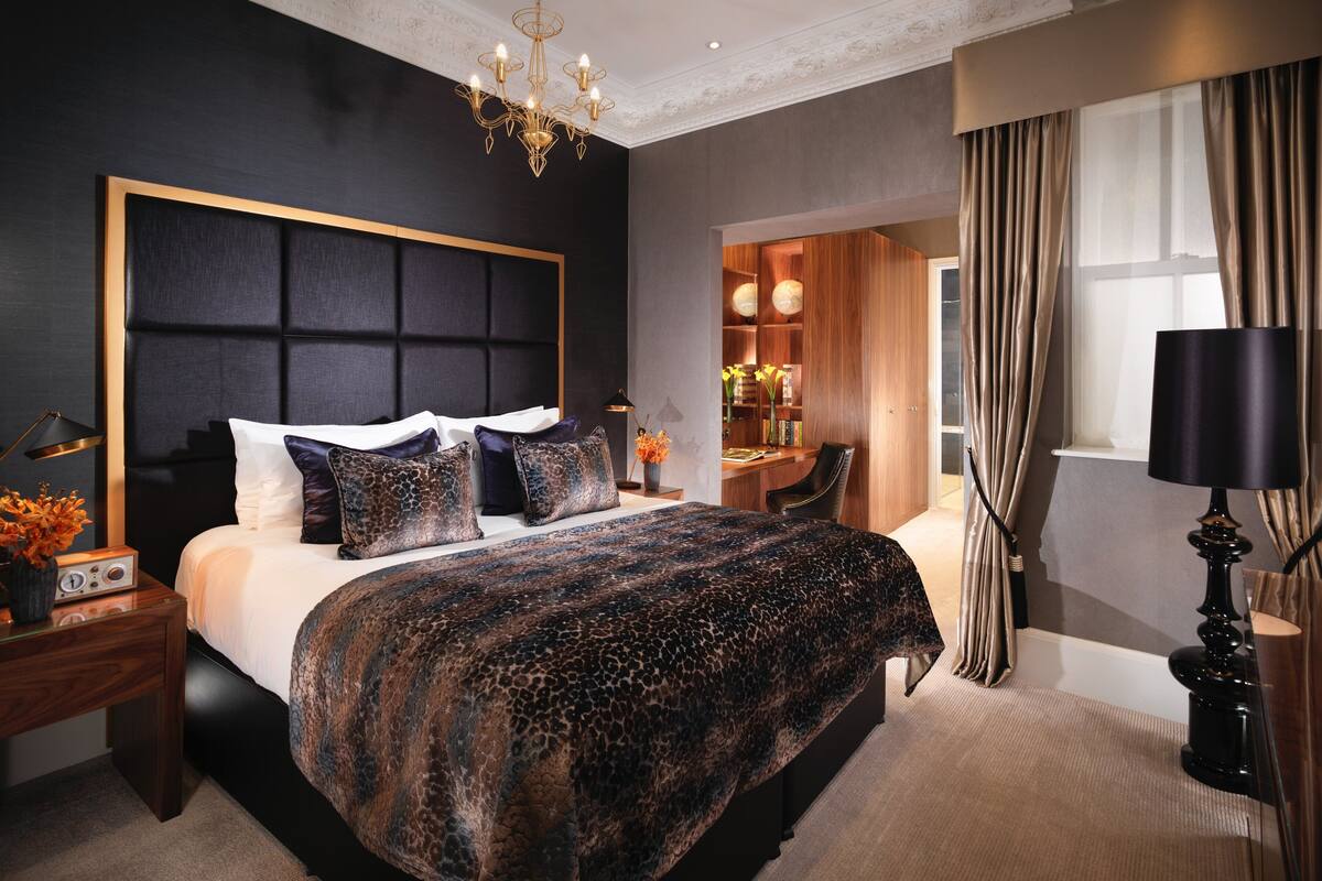 A modern bedroom with a large bed, a chandelier, a desk, and a TV.
