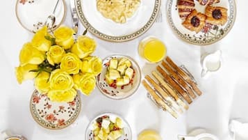 Una colazione servita con piatti di cibo, un vaso di fiori gialli e un teiera.