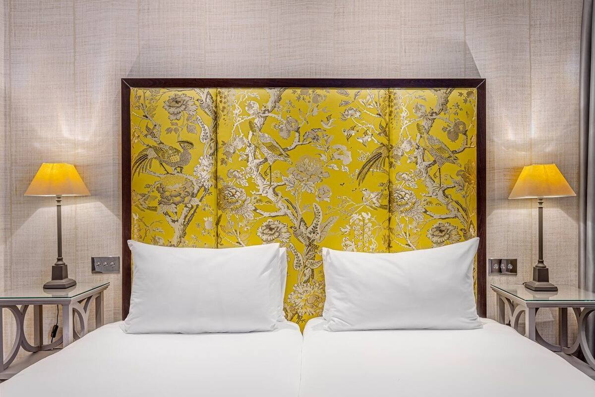 A hotel room with a large bed, two bedside lamps, and a decorative headboard with a floral pattern.