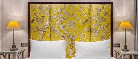 A hotel room with a large bed, two bedside lamps, and a decorative headboard with a floral pattern.