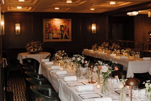 A formal dining room with tables set for service, featuring floral centerpieces and elegant tableware.