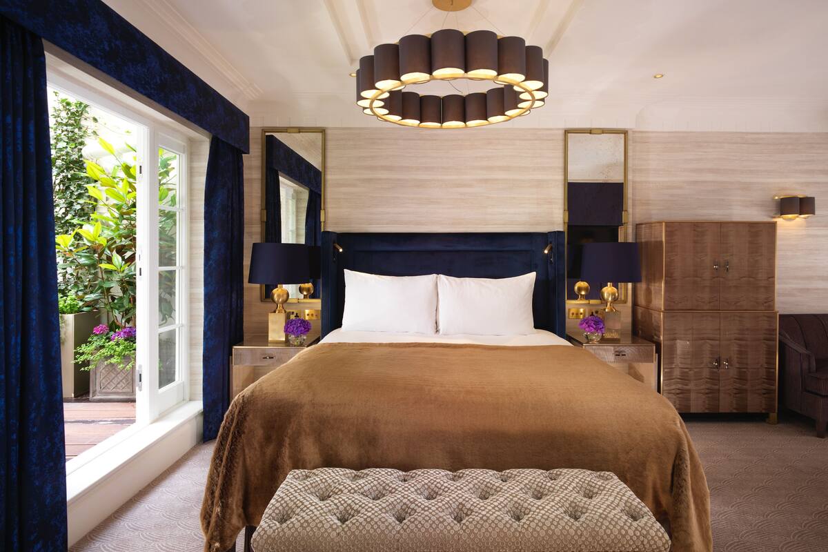 A hotel room with a large bed, a bench, a nightstand with lamps, a mirror, and a wardrobe.