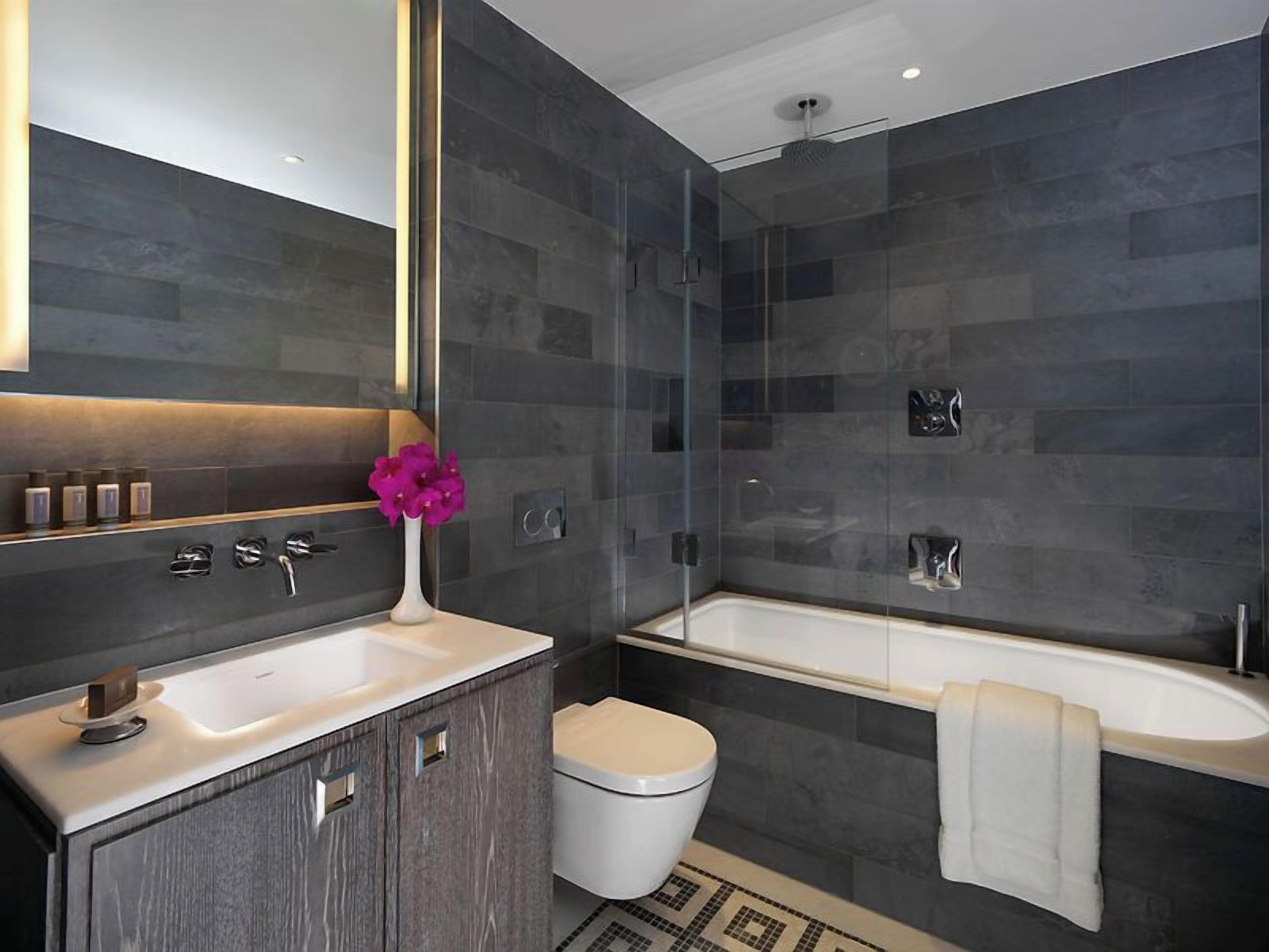 A modern bathroom with a glass-enclosed shower, a white bathtub, and a vanity with a mirror.