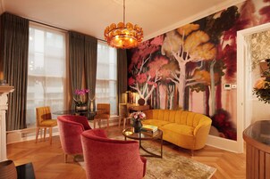 A living room with a yellow sofa, red armchairs, a round coffee table, and a large floral mural on the wall.
