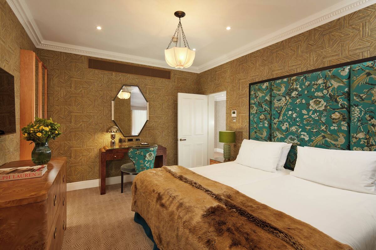 A bedroom with a large bed, a wooden dresser, a desk, and a mirror.