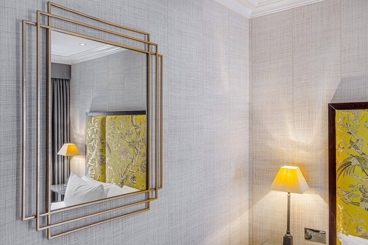 Habitación de hotel con un espejo grande, una lámpara de noche y papel tapiz floral.
