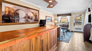 A reception area with a wooden reception desk, a flat-screen TV, a framed picture on the wall, and a view of the outside through a glass door. - Best Western University Lodge (Davis)