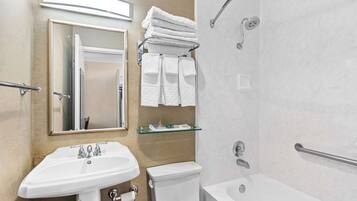 Une salle de bain moderne avec un lavabo, des toilettes et une baignoire. Des serviettes sont pliées et empilées sur une étagère, et il y a une cabine de douche en verre.